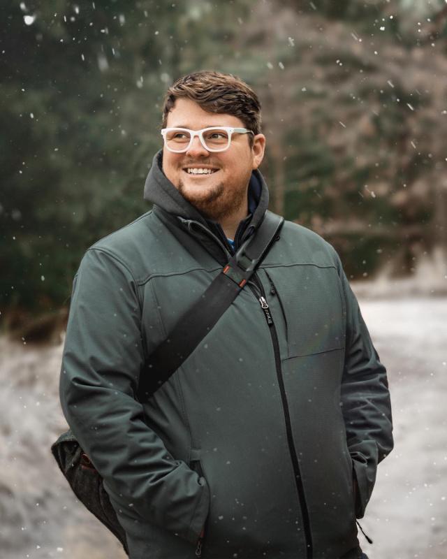 Corey Collins, photographer, smiling outdoors as snow falls in a Michigan winter.